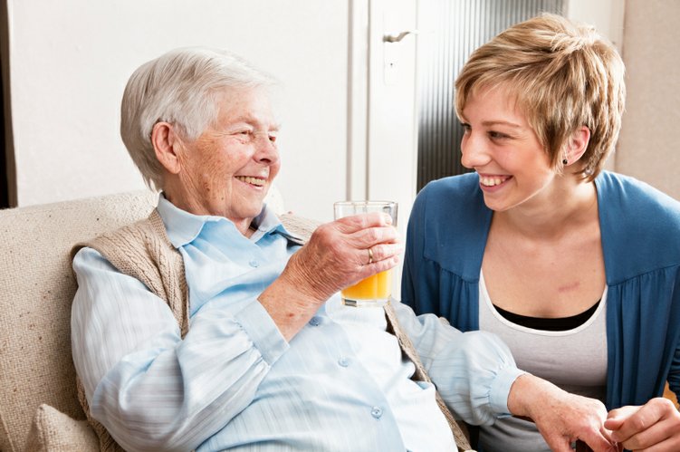 A middle aged woman smiling and holding hands with a elderly woman.